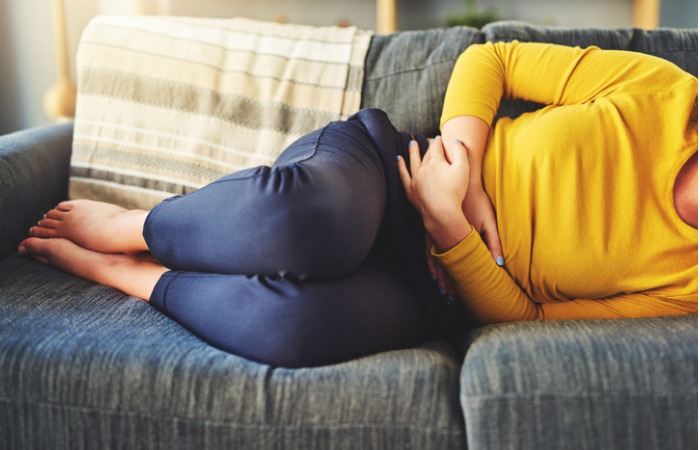 female laying on couch, hands holding abdomen