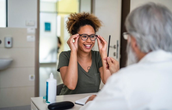 African American female trying on glasses while ophthalmologist sits in front of her