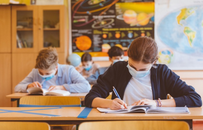 Students sitting in classroom, working on school work and wearing masks