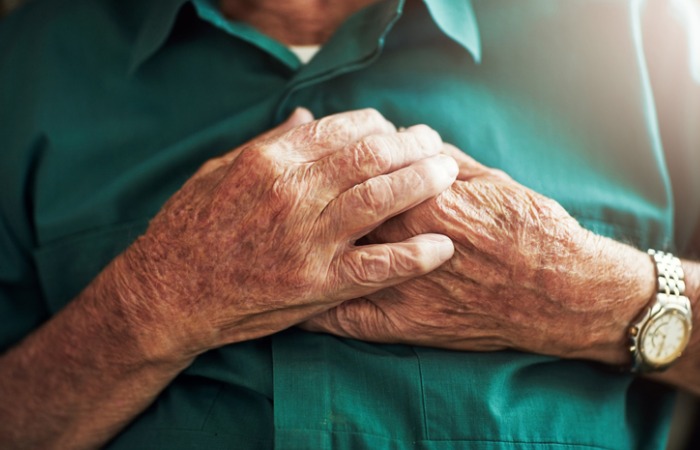 Unidentifiable elderly male holding hands over heart