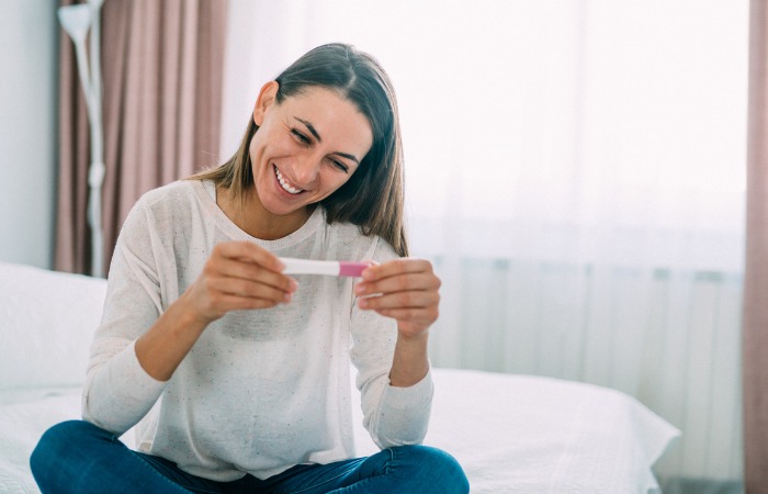 Brunette female smiling while sitting down and looking at the results of a pregnancy test