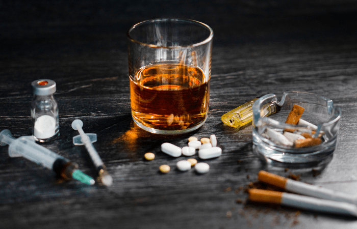 Variety of syringes, pills, alcohol, and cigarettes on a table