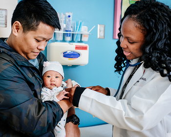 Father holding baby girl while doctor examines her