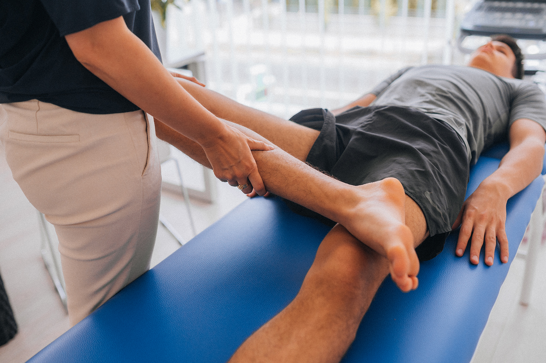 Female physiotherapist bending the knee of an injured male patient lying on a massage bed in the clinic