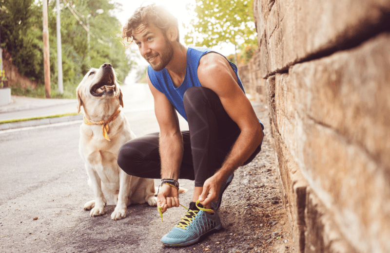 Male runner tying his shoe on the sidewalk next to his dog