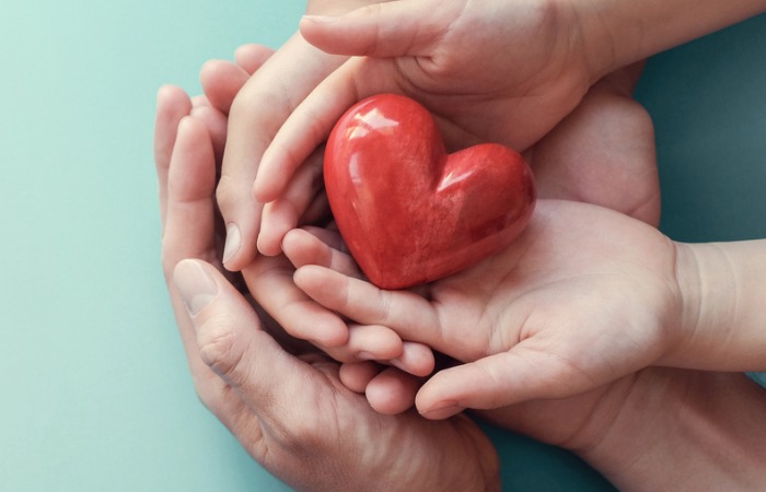 Three pairs of hands holding a heart-shaped figurine