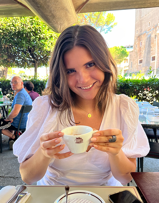 Laura Melton sitting at a cafe, smiling and holding up a cup of coffee