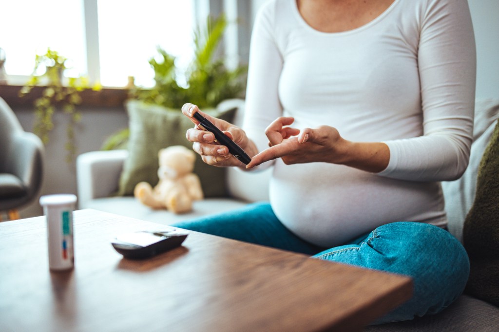 Happy Pregnant woman with glucometer checking blood sugar level at home.