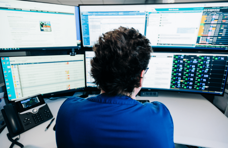 Employee sitting at desk, viewing several monitors in front of her