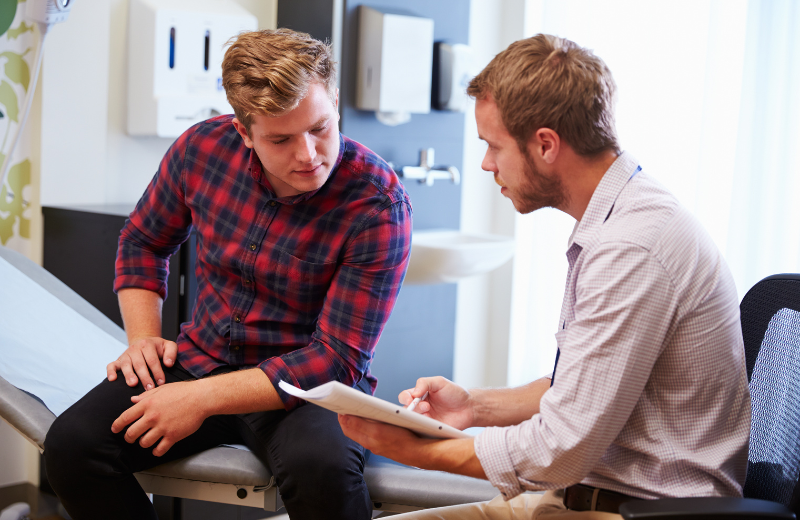 White male patient in flannel shirt speaking with a white male physician in a patient exam room