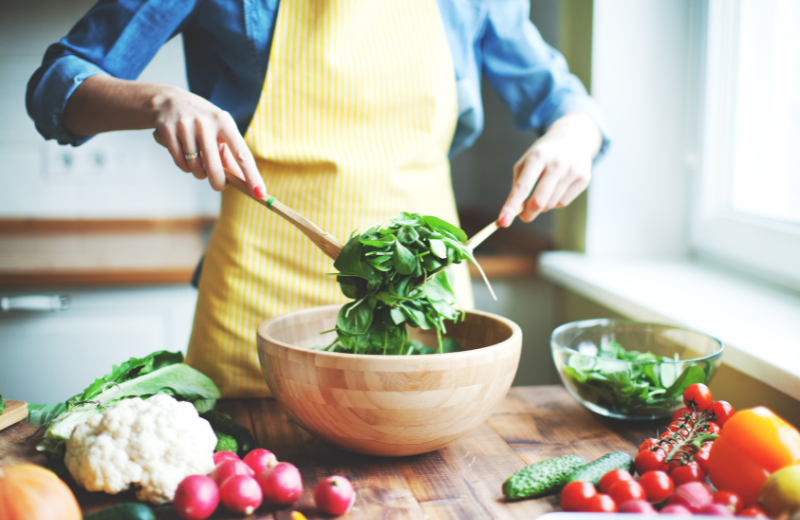 Individual mixing salad in a bowl, surrounded by fresh vegetables