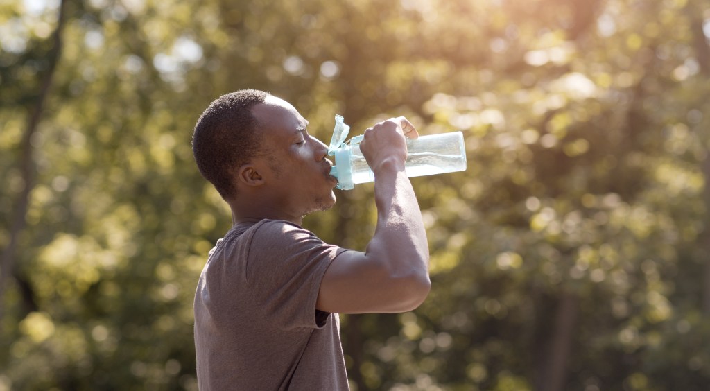 Overheated male drinking water from bottle in park