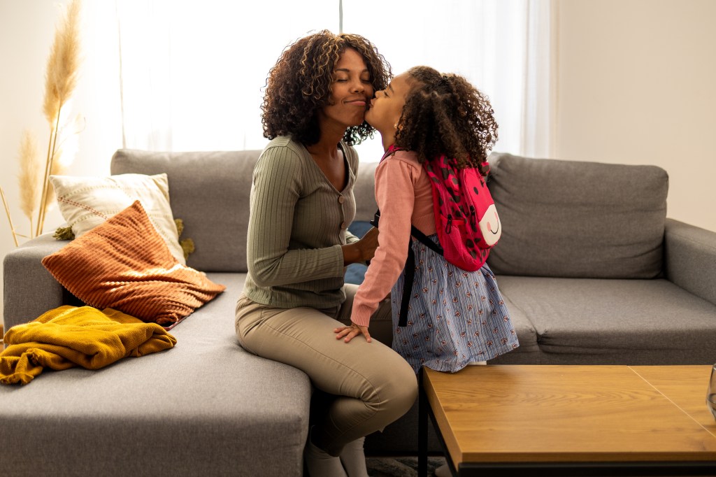 Beautiful young African American mother preparing her little daughter for school