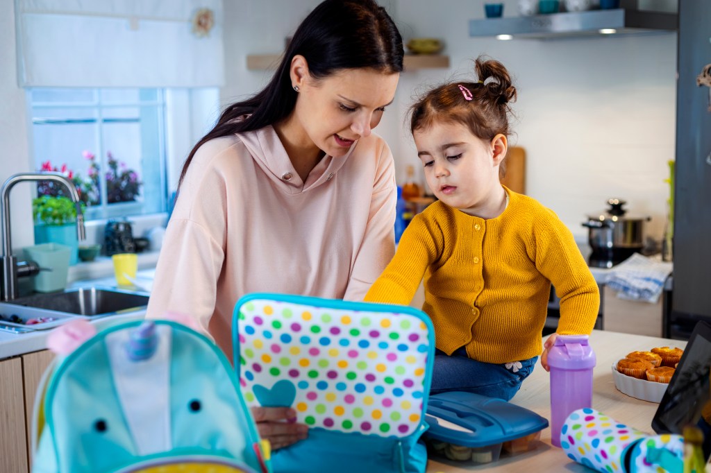 The cute little girl helps her mother to pack lunch and water for kindergarten together.