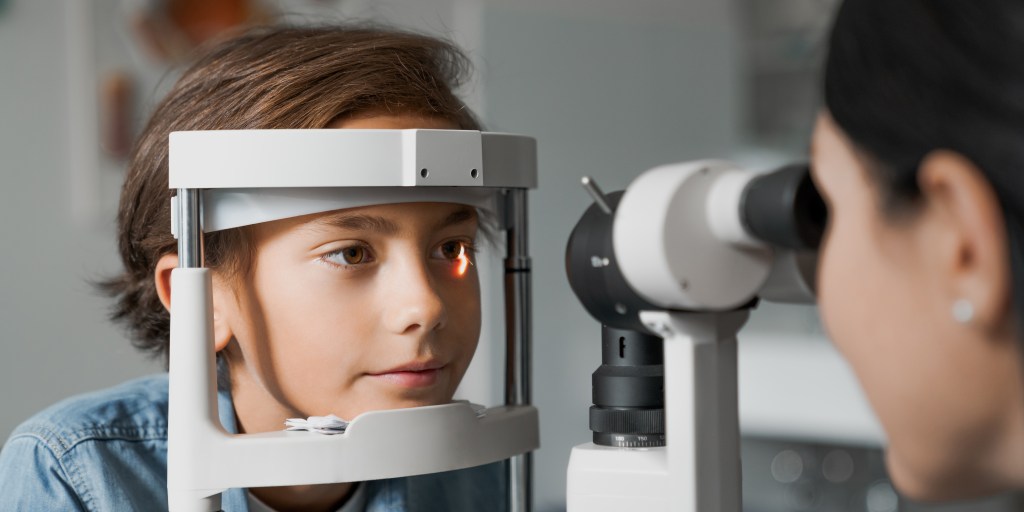 Adult female doctor ophthalmologist is checking the eye vision of cute child in modern clinic