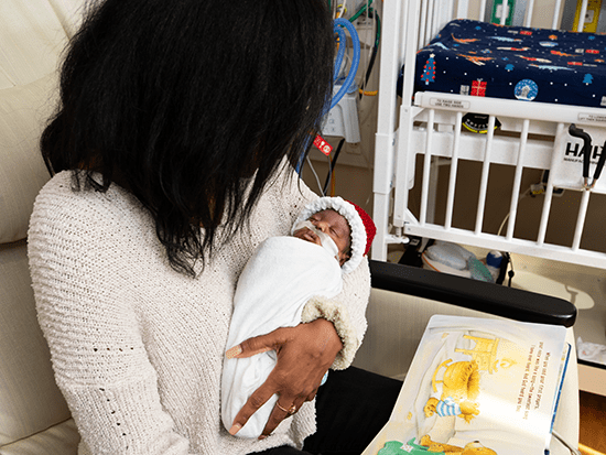 women holding newborn in UAB NICU with a book from the new book vending machine