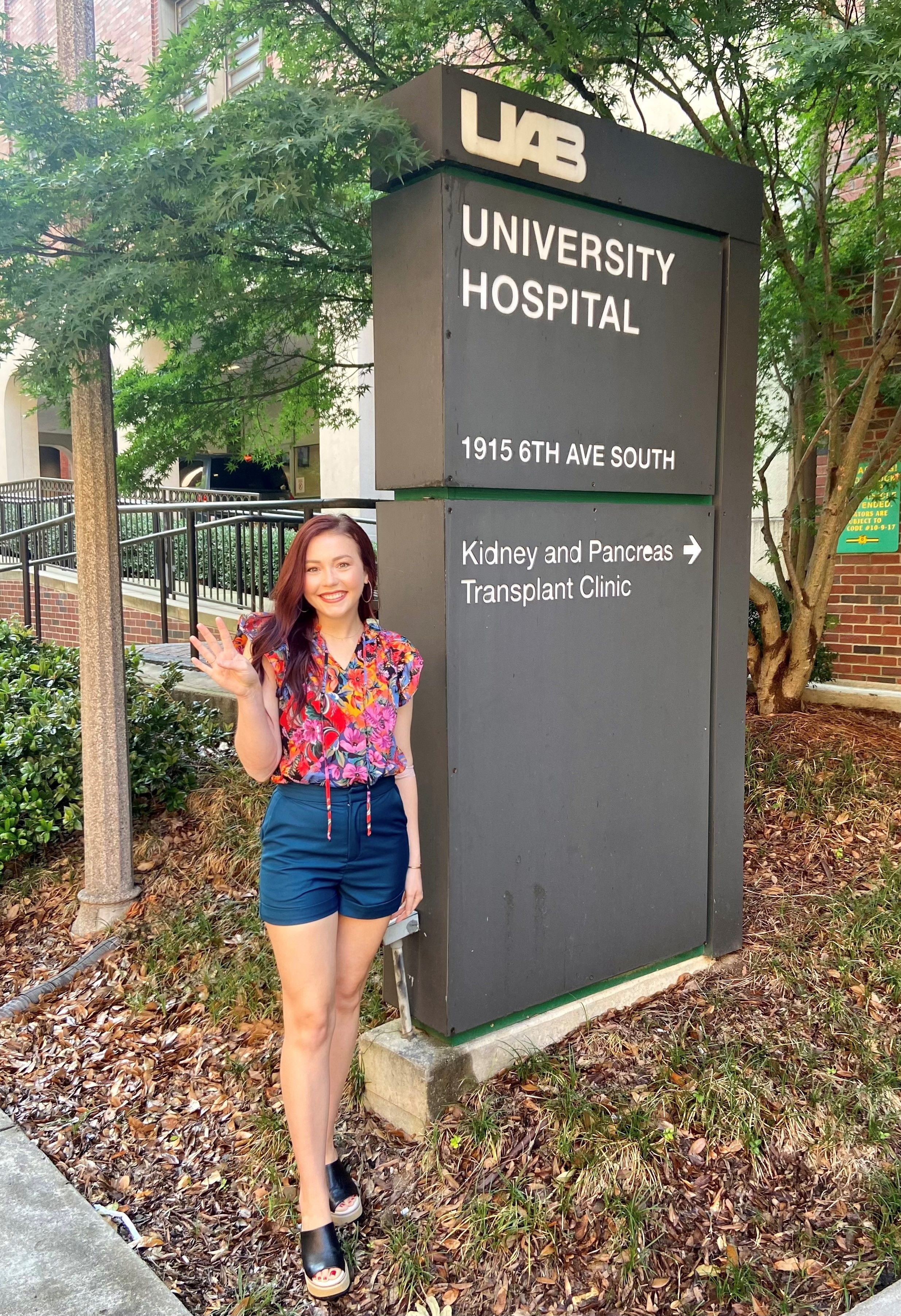 Ashley Nichols standing in front of the University Hospital sign for the Kidney and Pancreas Transplant Clinic